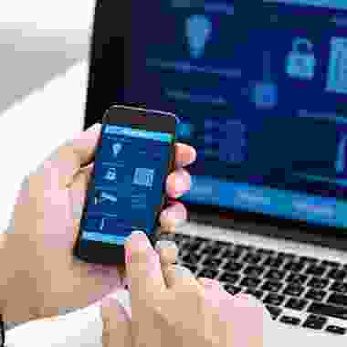 A person holding an iphone in front of a laptop.