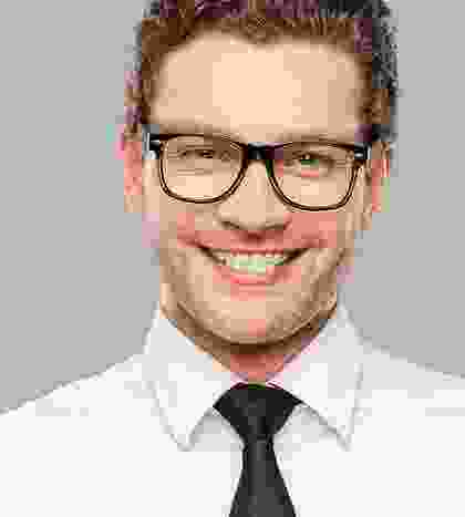 A man with glasses and a tie smiling.