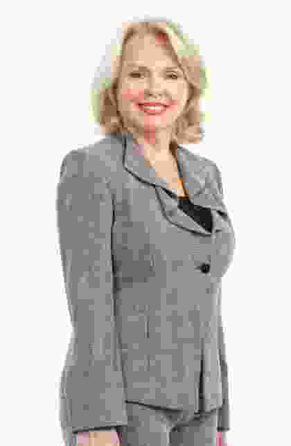 A woman in grey jacket standing next to wall.