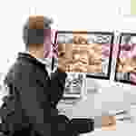 A man sitting in front of three computer screens.