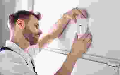 A man is holding the remote control for an air conditioner.