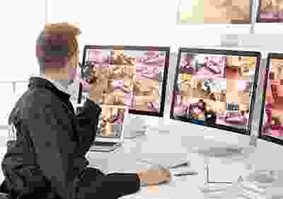 A woman sitting at her computer desk looking at three monitors.