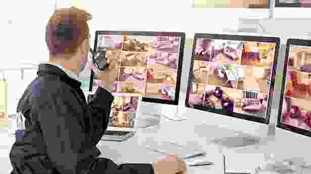 A man sitting in front of three computer screens.