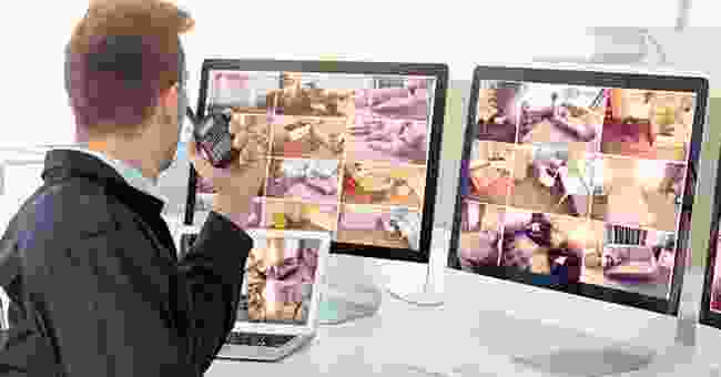 A person holding a cell phone in front of two computers.