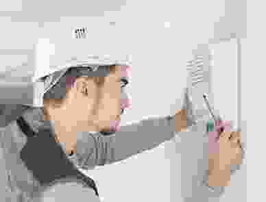 A man in white hard hat holding scissors and looking at the wall.
