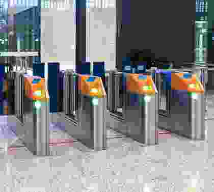 A row of silver and orange turnstiles in front of a building.