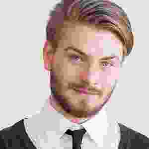 A man with long hair and beard wearing a black tie.