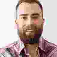 A man with a beard and mustache wearing a pink shirt.