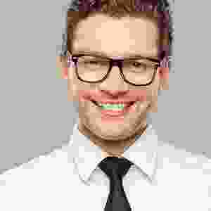 A man with glasses and a tie is smiling.
